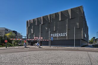 Seitenansicht auf die Fassade eines modernen Parkhauses mit Schriftzug Parkhaus und Schranken