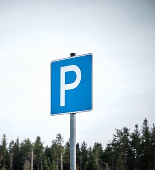Ein blaues Parkplatzschild vor Wald und Himmel