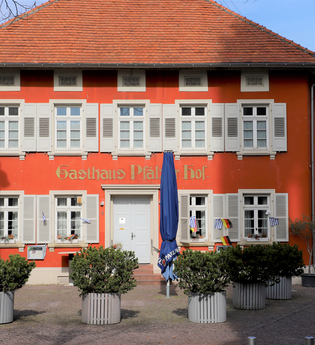 Rotes Gebäude des Gasthauses zur Pfalz mit grünen Pflanzen und blauen Schirmen