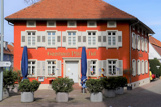 Rotes Gebäude des Gasthauses zur Pfalz mit grünen Pflanzen und blauen Schirmen