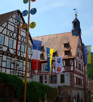 Blick auf das im Fachwerkstil errichtete Rathaus in Freudenberg. Im Vordergrund sind viele Fahnen zu sehen.