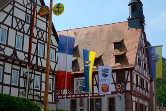 Blick auf das im Fachwerkstil errichtete Rathaus in Freudenberg. Im Vordergrund sind viele Fahnen zu sehen. | © Liebliches Taubertal