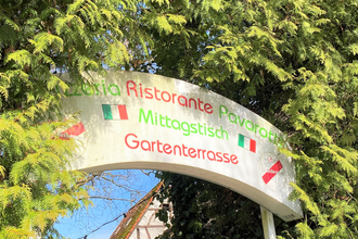 Schild "Pizzeria Ristorante Pavarotti" zwischen grünen Zweigen