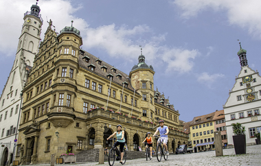 Blick auf das Rothenburger Rathaus. Auf dem Marktplatz davor ist eine Radlergruppe zu sehen.