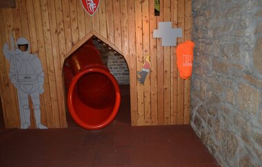 Blick auf einen Rutschenausgang in der Spielscheune in Röttingen. Der Ausgang ist mit einer Holzwand verkleidet. Ein gemalter Ritter hält daneben Wache. | © Tourismusverband "Liebliches Taubertal" e.V.