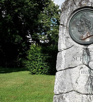 Schillerdenkmal im Schillergarten Gaildorf, umgeben von Bäumen und Rasen. | © Petra Natzkowski