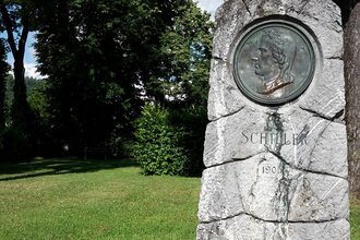 Schillerdenkmal im Schillergarten Gaildorf, umgeben von Bäumen und Rasen. | © Petra Natzkowski