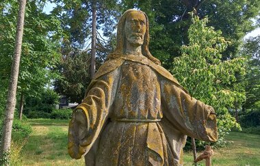 Steinfigur von Jesus im Schillergarten Gaildorf, umgeben von Bäumen. | © Petra Natzkowski