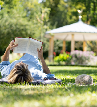 Eine Frag liegt mit auf der Wiese im Schlosspark und liest ein Buch. | © Björn Hänssler