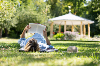 Eine Frag liegt mit auf der Wiese im Schlosspark und liest ein Buch. | © Björn Hänssler