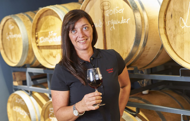 Eine Frau steht mit einem Rotwein vor Weinfässern | © Touristikgemeinschaft Hohenlohe e. V. | Weingut Schneckenhof