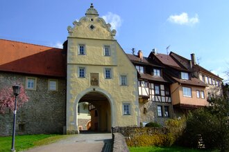 Das Tor ist gelb und hat einen Giebel. Daneben befinden sich Fachwerkhäuser auf der Stadtmauer | © Touristikgemeinschaft Hohenlohe e. V. | Stadt Forchtenberg