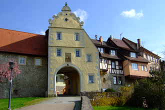 Das Tor ist gelb und hat einen Giebel. Daneben befinden sich Fachwerkhäuser auf der Stadtmauer | © Touristikgemeinschaft Hohenlohe e. V. | Stadt Forchtenberg