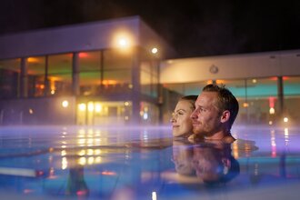 Ein Man und eine Frau sind im Mineralaußenbecken der Therme bei Nacht. | © Björn Hänssler
