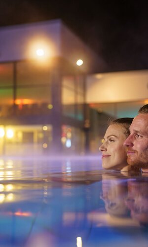Ein Man und eine Frau sind im Mineralaußenbecken der Therme bei Nacht. | © Björn Hänssler