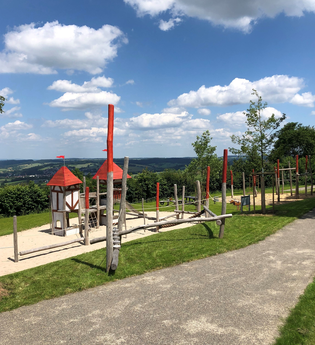 Hölzerne Klettergeräte mit rotem Dach auf sandigem Boden und Rasen