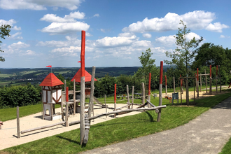 Hölzerne Klettergeräte mit rotem Dach auf sandigem Boden und Rasen