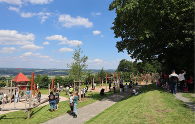 Zahlreiche Menschen auf einer Rasenfläche eines Spielplatzes an einem Sommertag