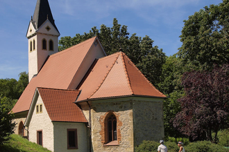 Zwei Radfahrer stehen vor einer Kapelle mit einem spitzen Turm | © Touristikgemeinschaft Hohenlohe e. V. | Susanne Schleussner