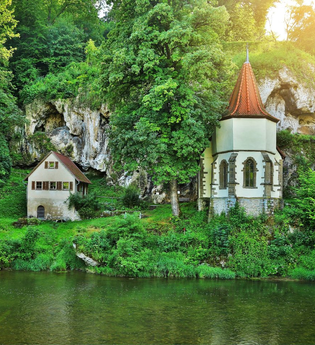 Die Wallfahrtskapelle steht am Fluss Jagst mit einer aufragenden Tuffsteinfelsenwand dahinter | © Touristikgemeinschaft Hohenlohe e. V. | Andi Schmid