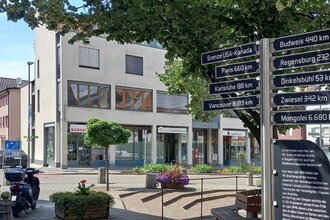Marktplatz mit Hinweistafel und Wegweiser zum 49. Breitengrad, im Hintergrund das moderne weiße Gebäude der Rathaus Außenstelle am Marktplatz 9 | © Petra Natzkowski