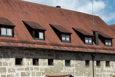 Stadtbücherei - langgezogenes, gemauertes Gebäude mit zahlreichen kleinen Fenstern, rotes Ziegeldach mit Dachgauben, rechts im Hintergrund die Fachwerkfassade des Alten Schlosses | © Stadt Gaildorf