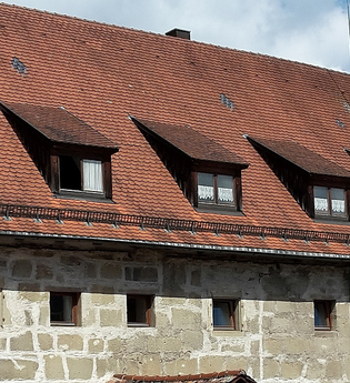 Stadtbücherei - langgezogenes, gemauertes Gebäude mit zahlreichen kleinen Fenstern, rotes Ziegeldach mit Dachgauben, rechts im Hintergrund die Fachwerkfassade des Alten Schlosses | © Stadt Gaildorf