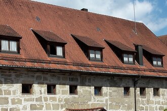 Stadtbücherei - langgezogenes, gemauertes Gebäude mit zahlreichen kleinen Fenstern, rotes Ziegeldach mit Dachgauben, rechts im Hintergrund die Fachwerkfassade des Alten Schlosses | © Stadt Gaildorf