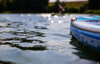 Nahaufnahme eines blauen SUP-Boards auf einem ruhigen See mit glitzerndem Wasser und unscharfen Ufern. | © Holger Hage für "Das Bergische"