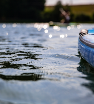 Nahaufnahme eines blauen SUP-Boards auf einem ruhigen See mit glitzerndem Wasser und unscharfen Ufern. | © Holger Hage für "Das Bergische"