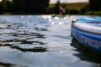 Nahaufnahme eines blauen SUP-Boards auf einem ruhigen See mit glitzerndem Wasser und unscharfen Ufern. | © Holger Hage für "Das Bergische"
