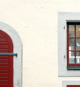 Eingangstüre zur Touristinformation aus dunkelrot gestrichenem Holz, rechts daneben zwei, dunkelrot gestrichene Sprossenfenstertüre, | © Petra Natzkowski