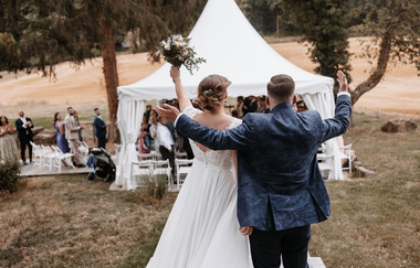 Brautpaar hebt die Arme vor den Gästen im Zelt | © Rottmann
