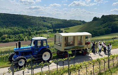 Traktor mit Planwagenanhänger auf der Straße zwischen den Reeben und einer kleinen Menschengruppe | © Ute Schmidt