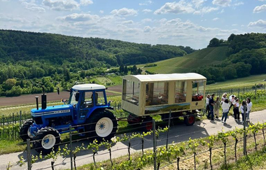 Traktor mit Planwagenanhänger auf der Straße zwischen den Reeben und einer kleinen Menschengruppe | © Ute Schmidt