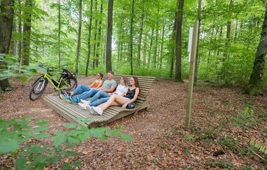 Vier Personen ruhen auf einem Waldsofa im Wald, ein Fahrrad lehnt daneben. | © Stadt Sinsheim