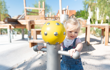Ein kleines Mädchen an einem Spielgerät mit gelbem Wassersprühkopf. Im Hintergrund sind unscharf weitere Spiel- und Klettergeräte zu erkennen. | © Stadt Eppingen