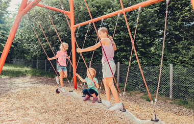 Drei Mädchen spielen auf einem Spielplatz auf einem hängenden Schwebebalken. | © Touristikgemeinschaft HeilbronnerLand e.V.