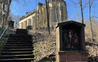 Blick auf den Weg und die Treppe hoch zur Bergkirche Laudenbach bei Weikersheim. Im Vordergrund ist eine Heiligenstatue zu sehen.