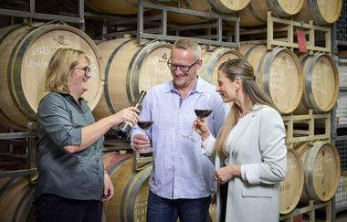 Drei Personen verkosten Wein im Weinkeller, mit Weinfässern im Hintergrund | © Touristikgemeinschaft Hohenlohe e. V.