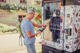 Ein Mann steht am Weinautomaten vom Weingut Koppenhöfer und hält eine Weinflasche in der Hand | © Tourismus im Weinsberger Tal e.V.