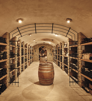 eleganter Gewölbekeller mit mehreren, gut bestückten, Weinregalen rechts und links. In der Mitte des Kellers steht ein Weinfass | © Weingut Albrecht-Kiessling