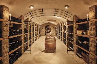 eleganter Gewölbekeller mit mehreren, gut bestückten, Weinregalen rechts und links. In der Mitte des Kellers steht ein Weinfass | © Weingut Albrecht-Kiessling