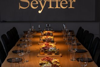 Tagungsraum mit goldenem Schriftzug an Wand "Seyffer", lange Holztafel, eingedeckt mit Essen in der Mitte | © Christian Seyffer