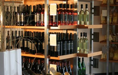 Regale mit Wein und regionalen Produkten stehen zum Verkauf bereit und davor liegen Weine in einem Korb mit Glas bereit für die Weinprobe | © Touristikgemeinschaft Hohenlohe e.V. | Weingut Ungerer