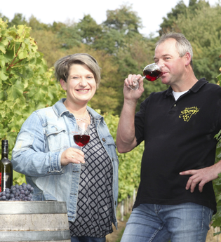 Eine Frau und ein Mann stehen in einem Weinberg bei einem Weinfass und halten ein Glas Rotwein in der Hand | © Touristikgemeinschaft Hohenlohe e. V. | Weinhof Dieroff