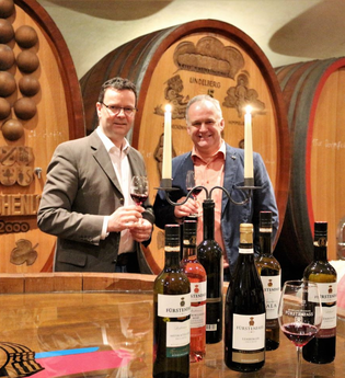 Zwei Männer halten ein Glas Wein in der Hand und stehen vor großen, schmucken Holzfässern | © Touristikgemeinschaft Hohenlohe e. V.