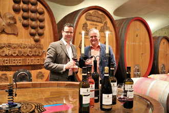 Zwei Männer halten ein Glas Wein in der Hand und stehen vor großen, schmucken Holzfässern | © Touristikgemeinschaft Hohenlohe e. V.