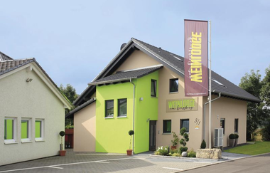 Gebäude von Außen zu sehen mit grünem und braunen Farben und einer großen Fahne im Vordergrund mit Weinlodge