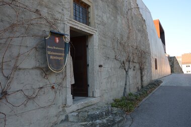 Blick auf den äußeren Eingangsbereich des Weinmuseums in Röttingen. An der Wand hängt ein großes Ritter-Schutzschild mit der Aufschrift "Burg Brattenstein, Weinmuseum Röttingen" . | © Stadt Röttingen